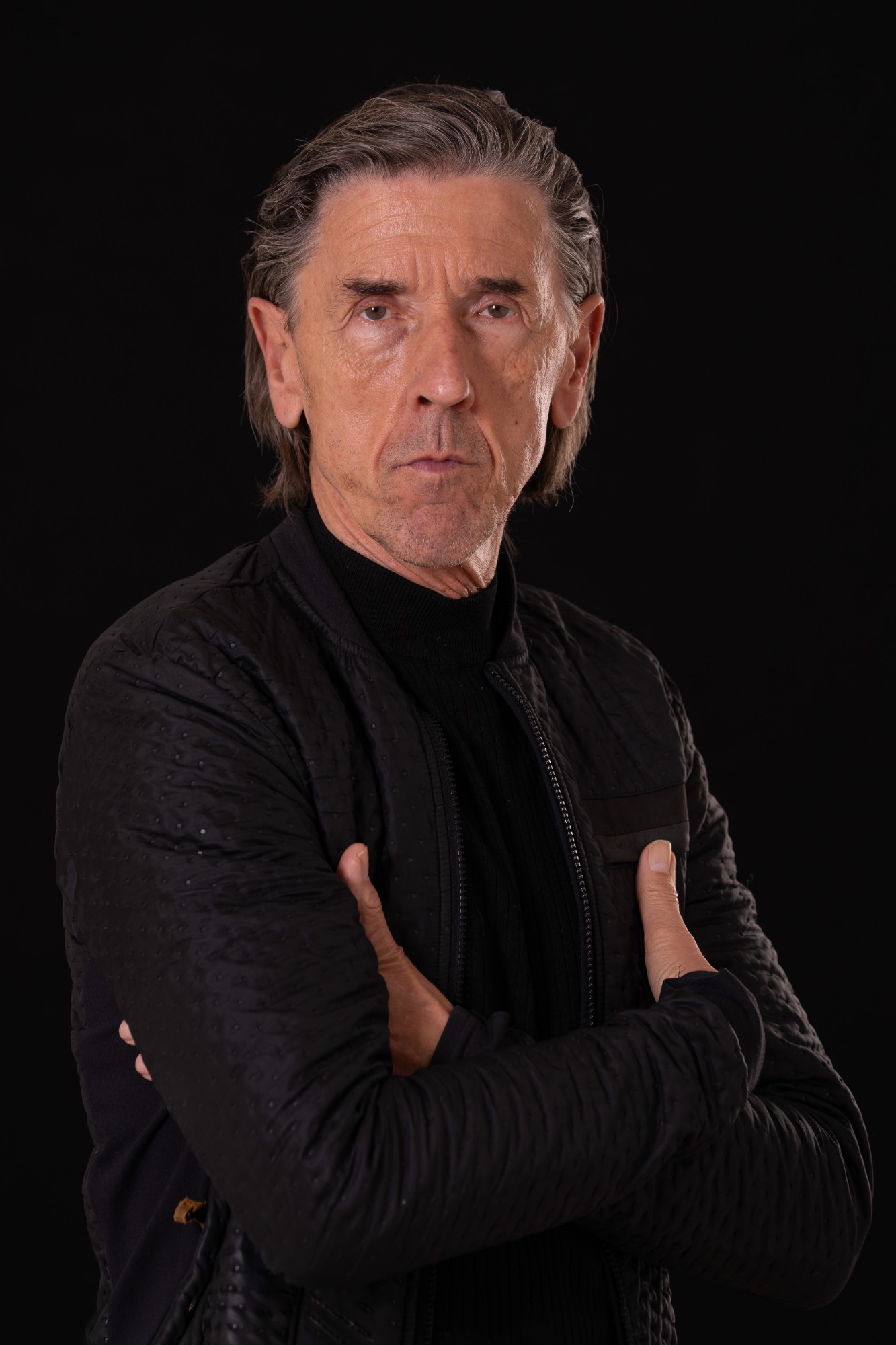 Uwe Koczulap mit verschränkten Armen in schwarzer Jacke vor schwarzem Hintergrund